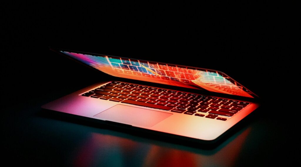 Laptop partially opened, emitting vibrant multicolored lights in dark setting.